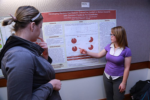 Female student presenting her research to another female student.