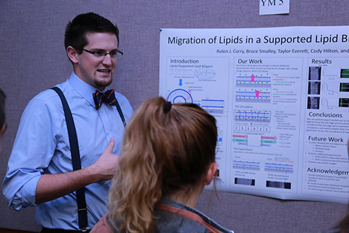 Male student in a bowtie explaining his research to other students.