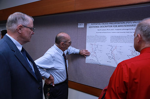 Threee older men surrounding a research poster.