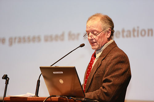 An older man speaking into a microphone and looking at his laptop.