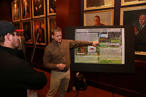 A man presenting information from his poster to an interested group.