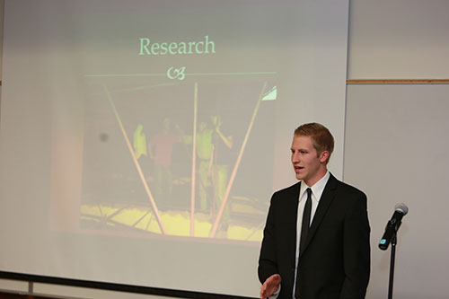 Presenter standing next to a microphone and a photo from his research project.