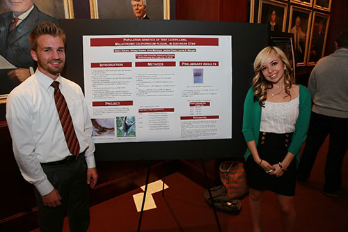A male and a female student standing next to their research poster.