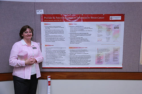 Lady in pink shirt standing by a breast cancer research poster.