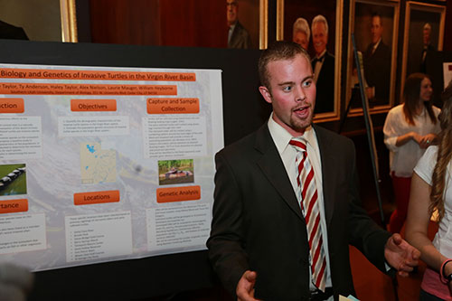 A man in a suit speaking next to his poster.