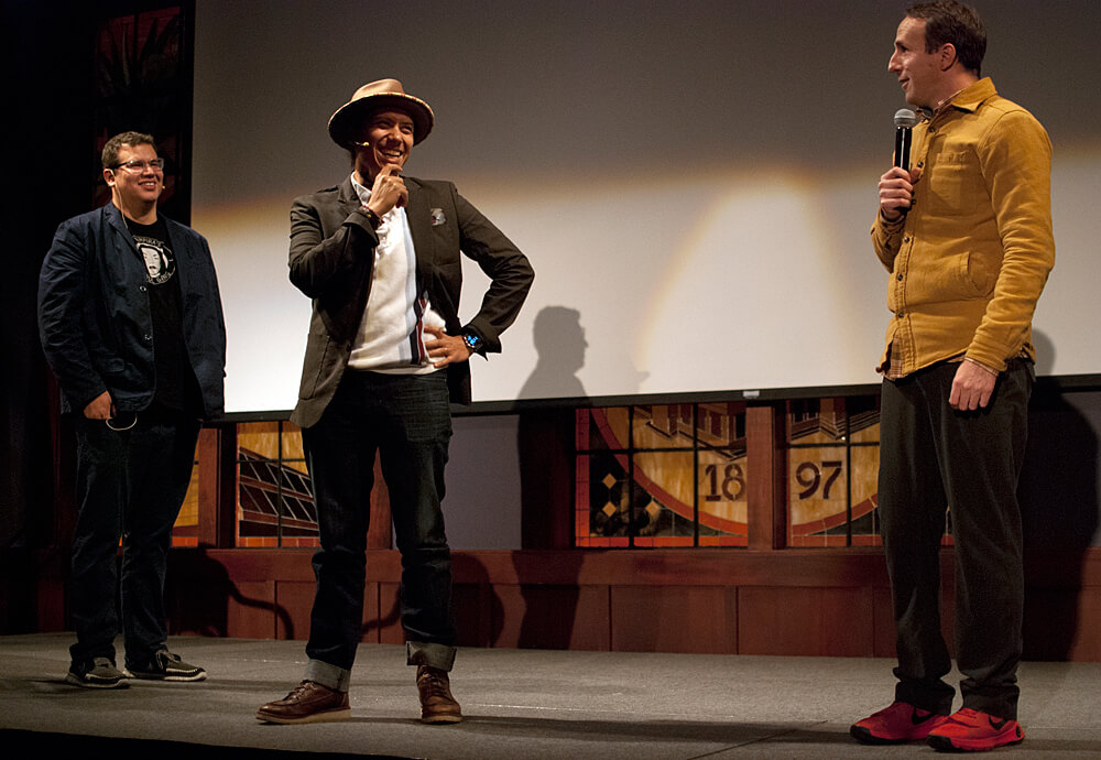 Three men standing onstage in conversation. 3