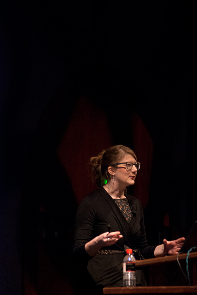Profile view of a woman speaking onstage. 6