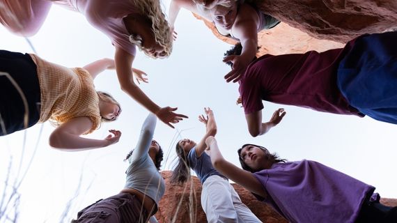 Photo of seven Dance students posing at Thunderbird Gardens. Photo is taken from the ground, looking up to the sky through their arms.