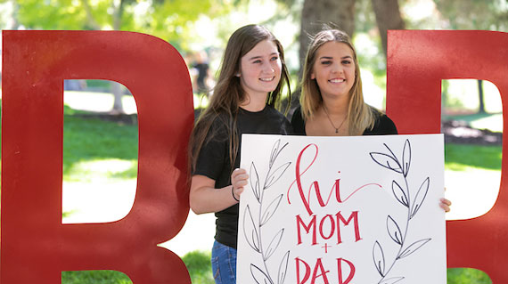students holding a sign that says "hi mom and dad"