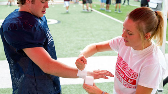 Student wrapping football players arm