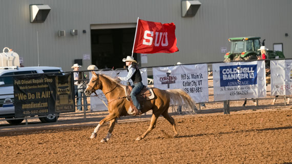 Student holding SUU flag while riding a horse