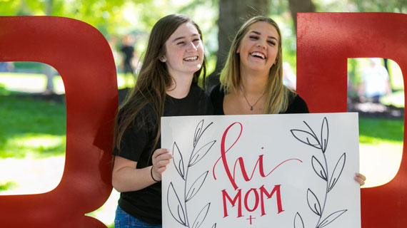 Two female students holding a "hi mom and dad" sign outside