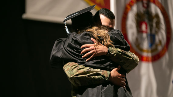 Student in cap and gown hugging man in army clothing