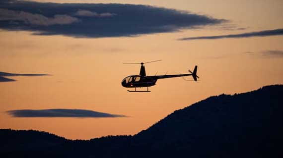 SUU helicopter flying against sunset backdrop, mountains beneath
