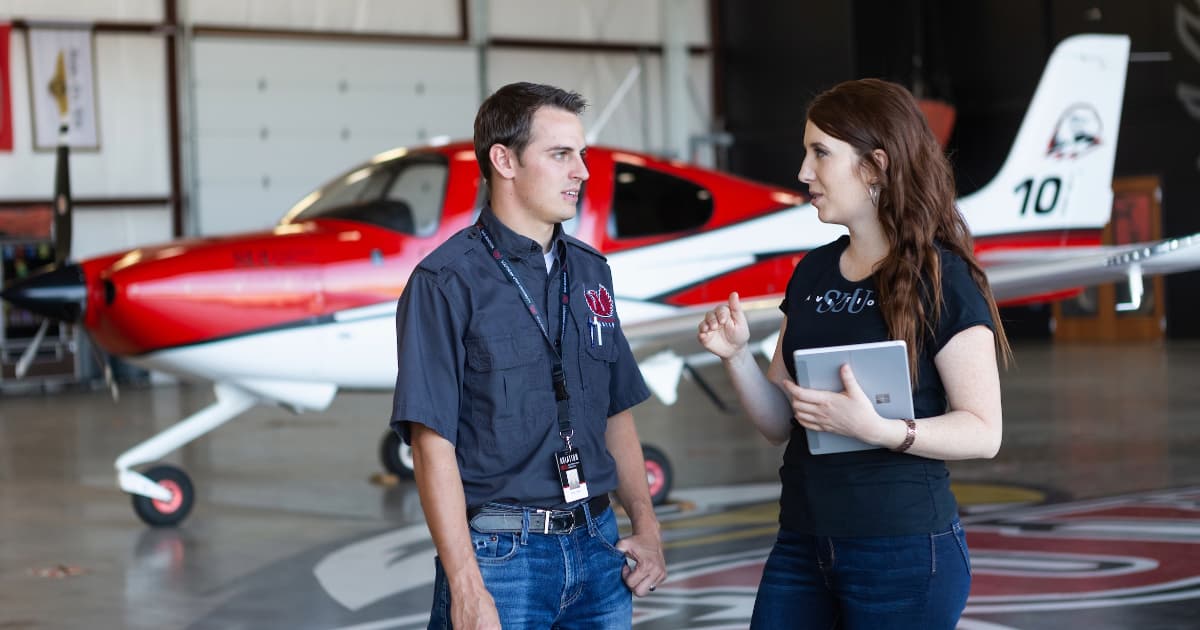 Aviation instructor and student talking in front of an airplane.