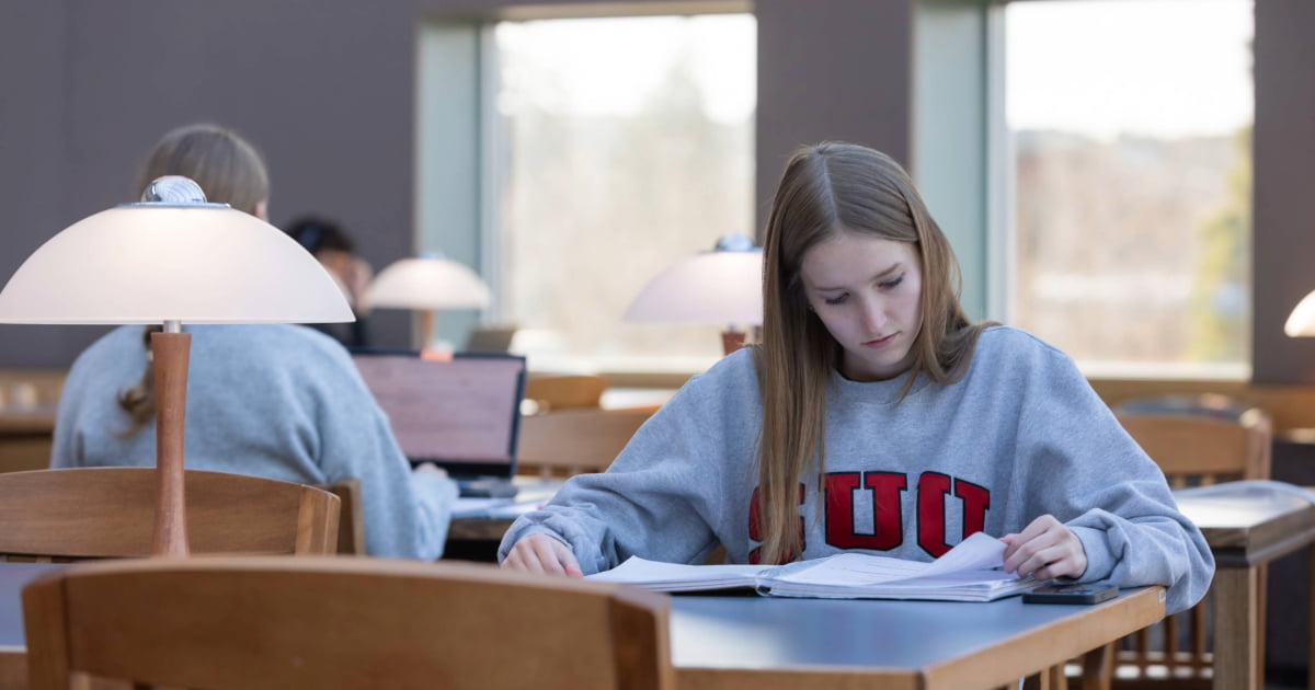 A student studying in the library on Southern Utah University campus. They are sitting at a table looking at a notebook.