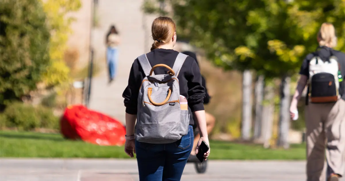 A young woman walks through SUU Campus with her back turned to the camera.