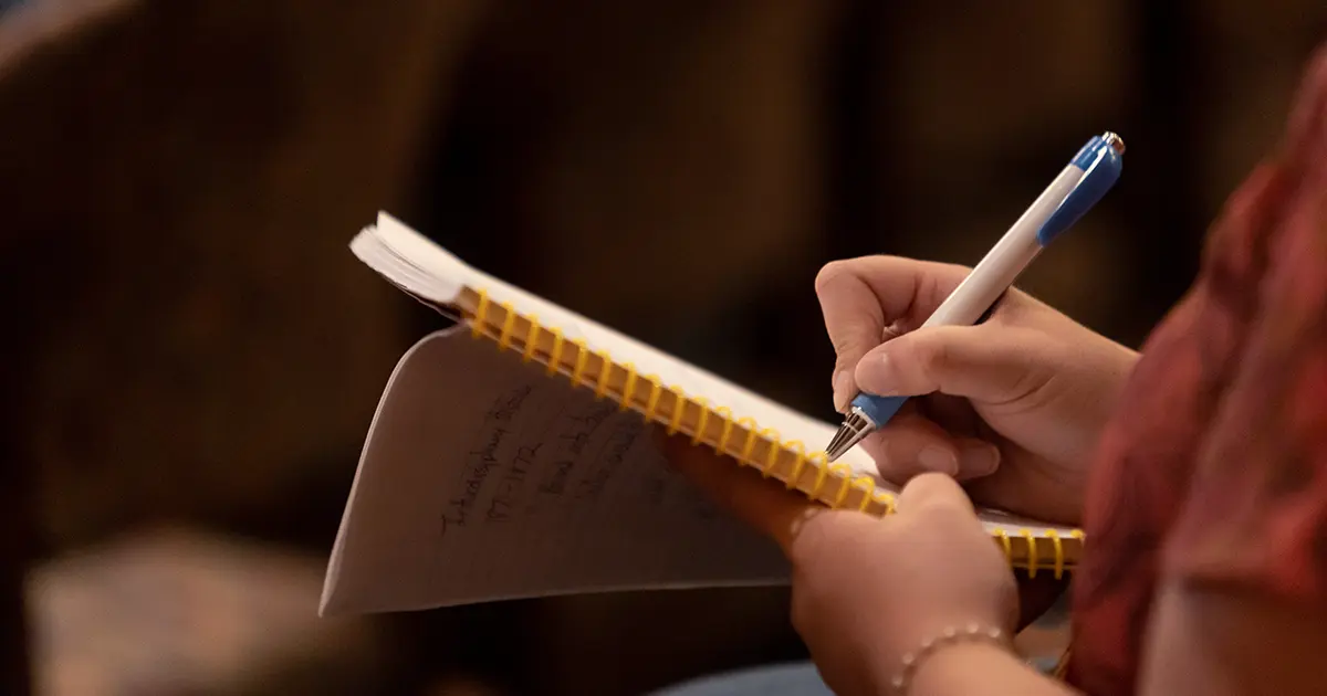 A person holding a notepad and writing with a pen