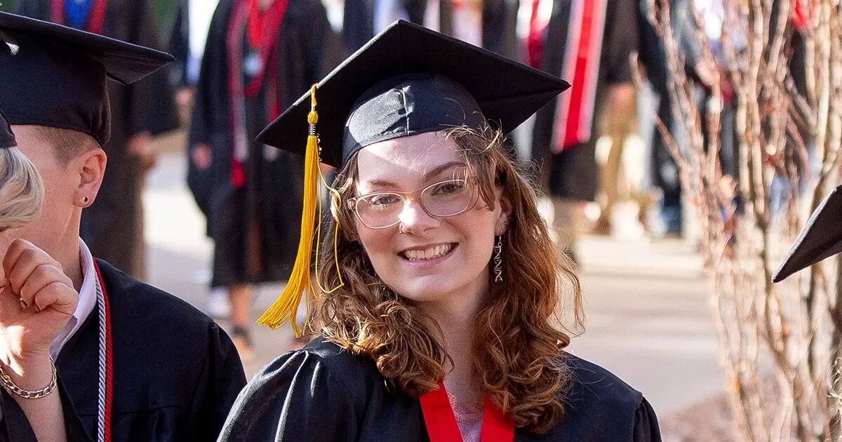 A woman in a graduating cap and gown smiles at the camera.