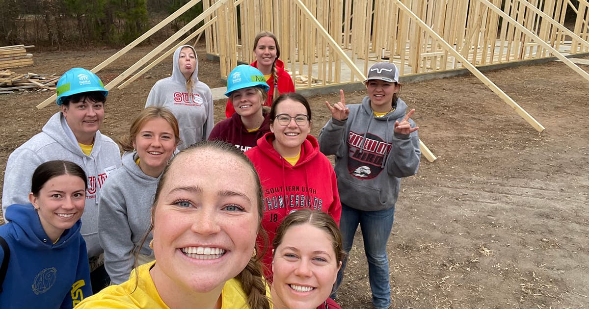 Students group together for a selfie in front of a partially built house frame