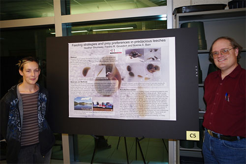 A man and a woman standing next to their research poster