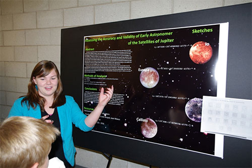 A female presenting a poster with planets depicted on it, as well as research information