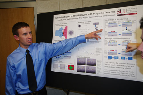 A male student pointing to a diagram on his research poster