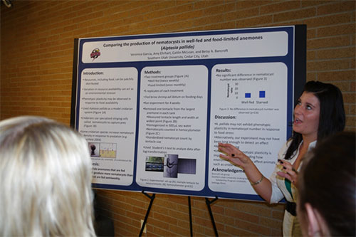 A female student presenting research information from her poster to two ladies