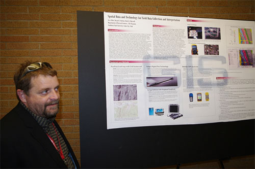 A man with sunglasses on his head standing next to a research poster