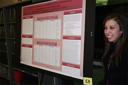 A female student standing to the side of a research poster.