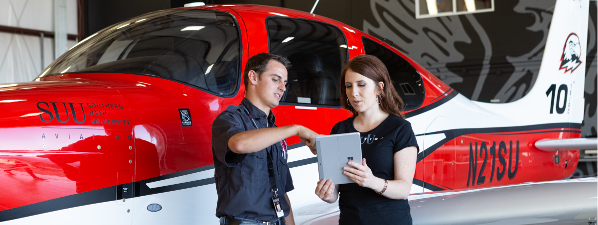 A student and a professor standing in front of an airplane.