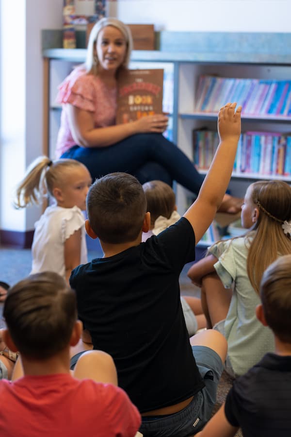 Elementary student raising his hand as the teacher is reading a book for the class