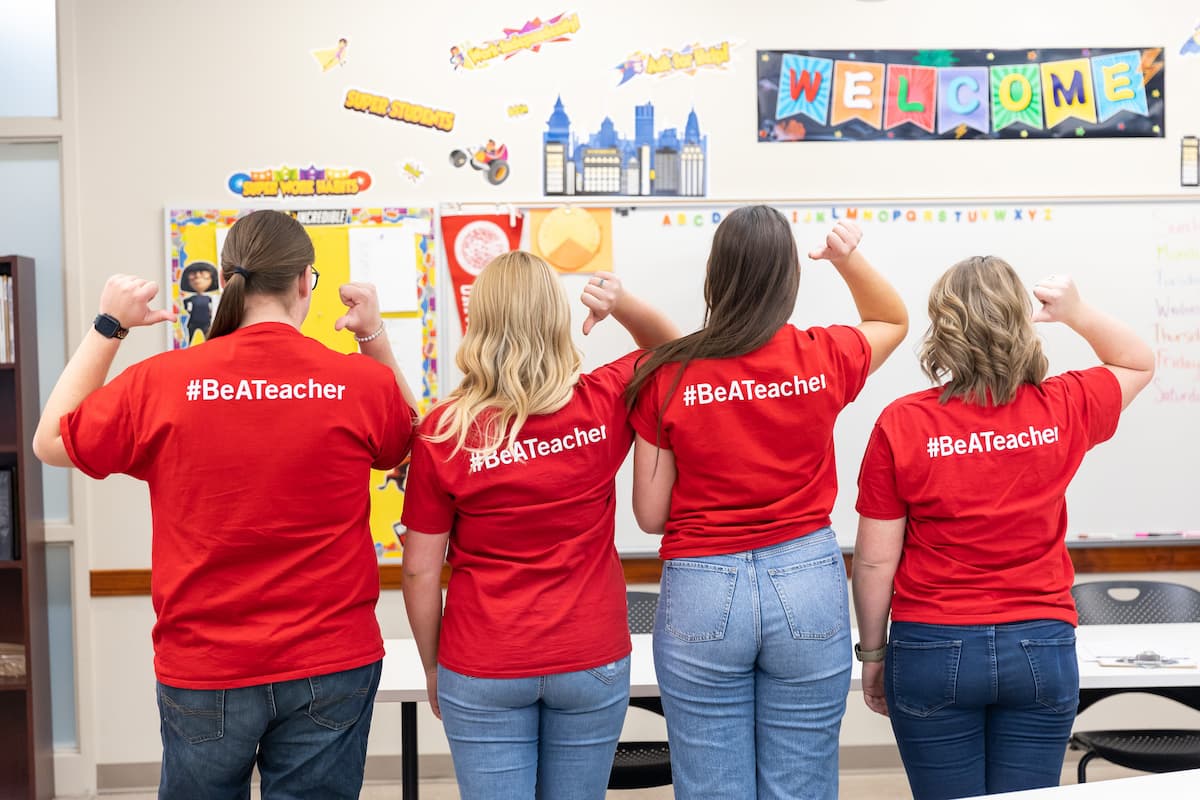 Four student teachers pointing to the text on the back of their shirts that says #BeATeacher