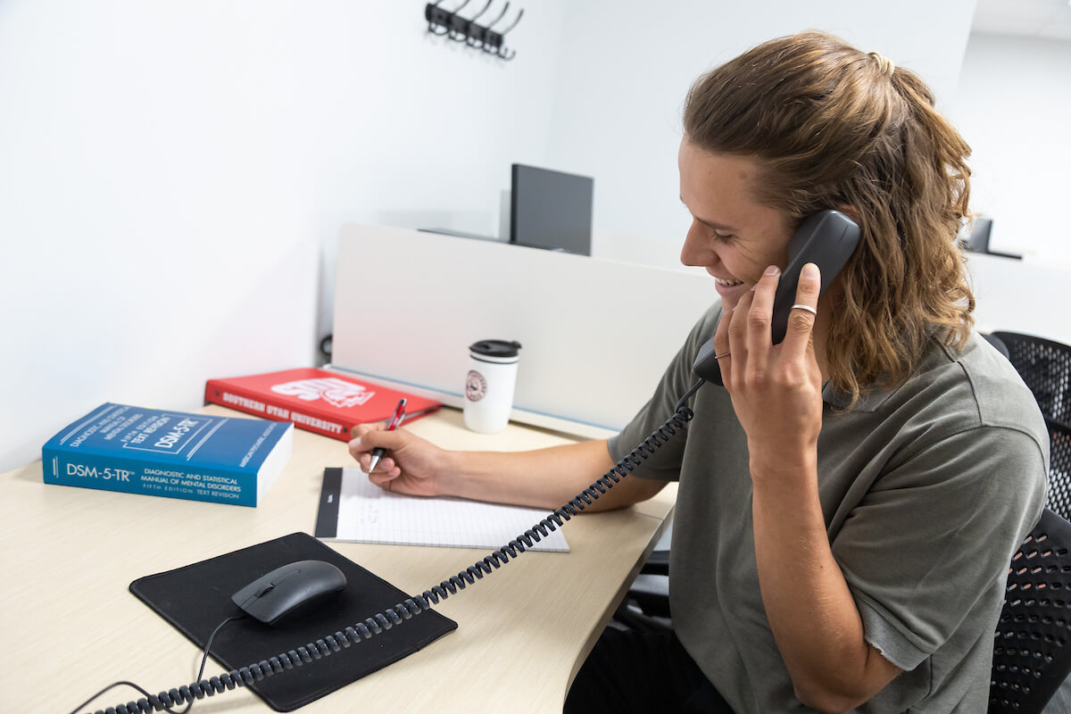 Young Student Worker speaking on a telephone and writing notes on a paper