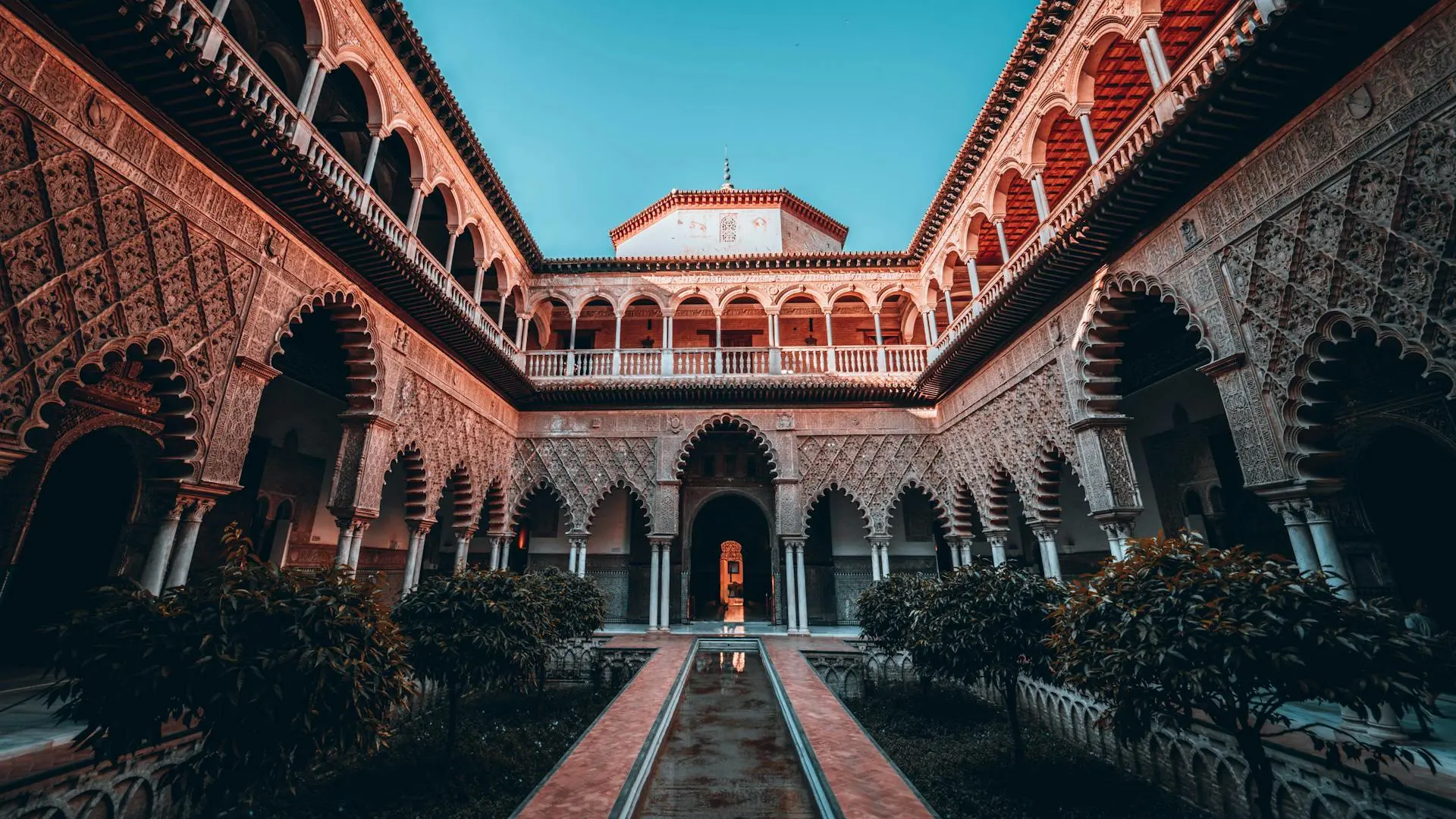 Alcázar palace in Seville Spain in the evening light. There are beautiful and intricate archways and trees line a walkway. 6