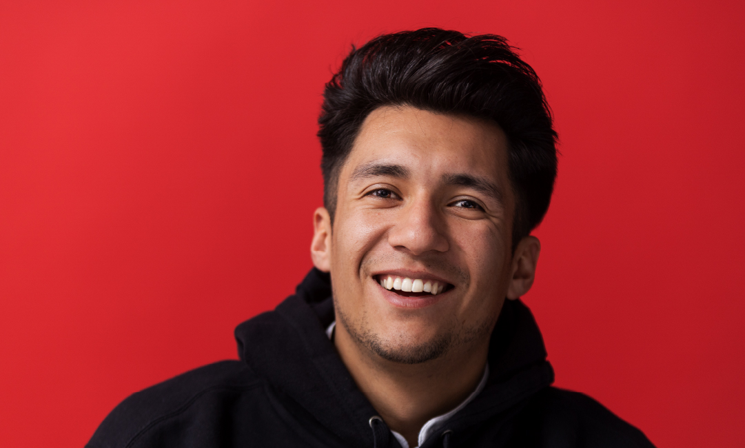 A student smiling against a pure red background.
