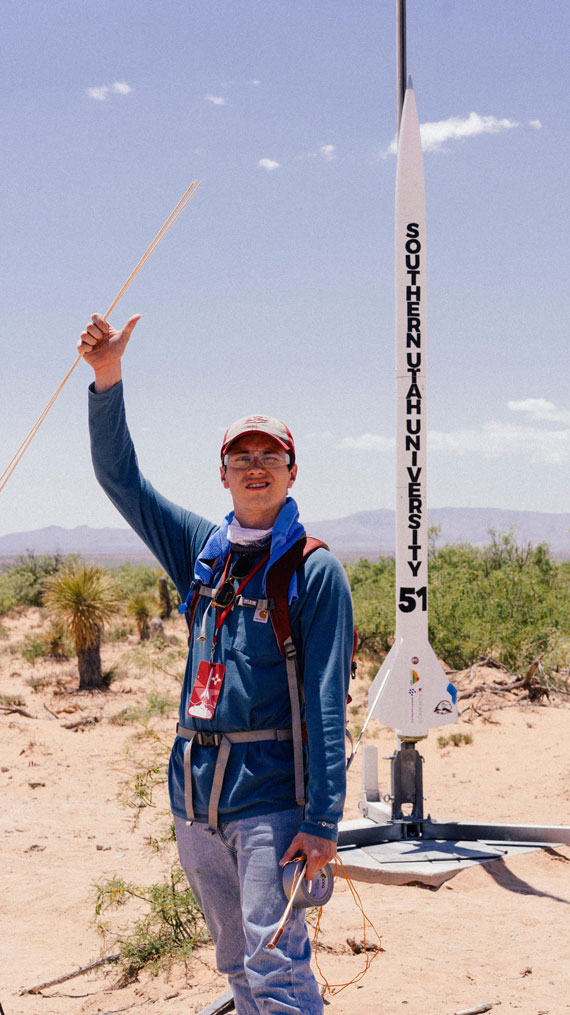 a student with their hand raised, standing in front of a rocket