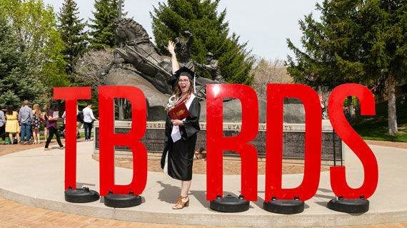 Student in cap and gown posing in front of t-bird letters