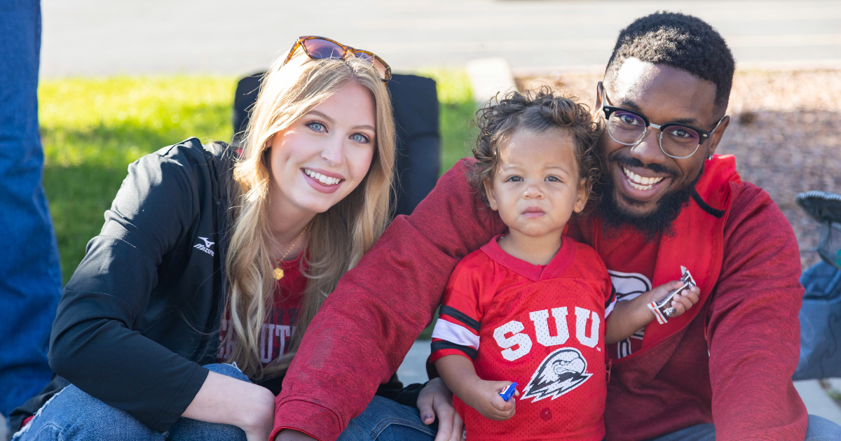 Mother, father, and daughter dressed in SUU colors smiling at the camera at the homecoming parade