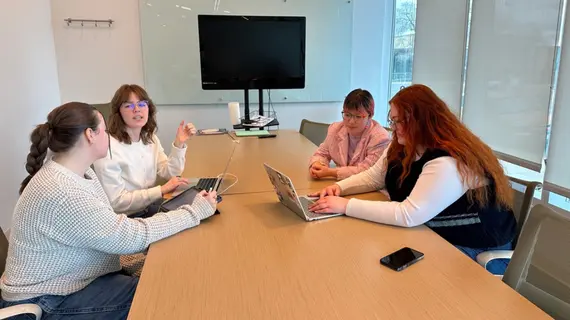 Four students sit at a conference table, preparing a presentation.