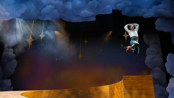 Photo from SUU's production of Pippin. An actor leaps on a stage decorated with stars and clouds.