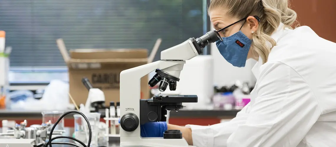A woman in a lab coat looking into a microscope