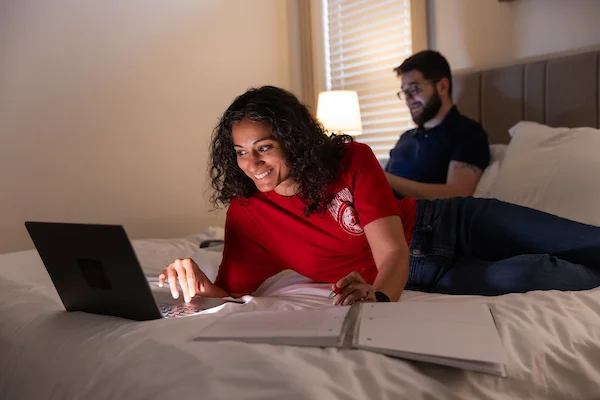 Woman laying on bed looking at laptop applying to enroll at SUU for the Let's GO graduate scholarship