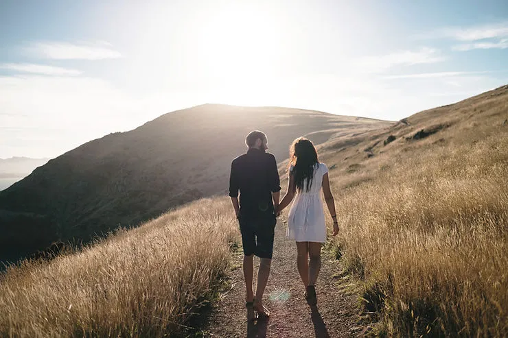 A photo of a man and woman holding hands as they walk up a path.