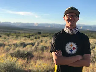 A portrait photograph of Kurt. There is tall grass, sagebrush, and yellow flowers in the background as well as distant mountains.