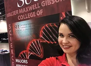 A selfie of Rachel who is smiling. A poster of SUU Walter Maxwell Gibson College of Science and Engineering is prominent in the background.
