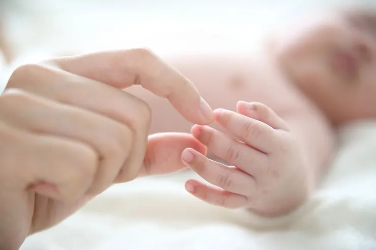 A close-up of an adult hand holding a baby’s hand.