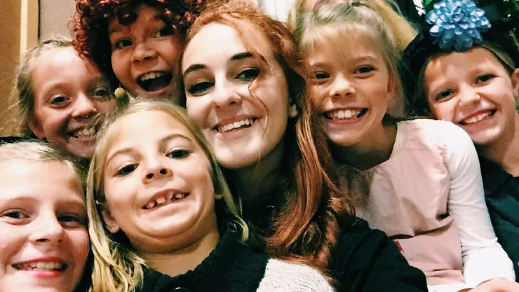 A group photograph of several children and a young adult, all smiling brightly.