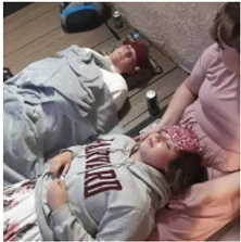 Two people are laying on the ground while being treated for a medical condition. A third person is holding one of the individuals heads in their lap.