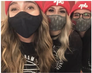 Three people are wearing masks and red hats while smiling, though you cannot see their lips due to the masks